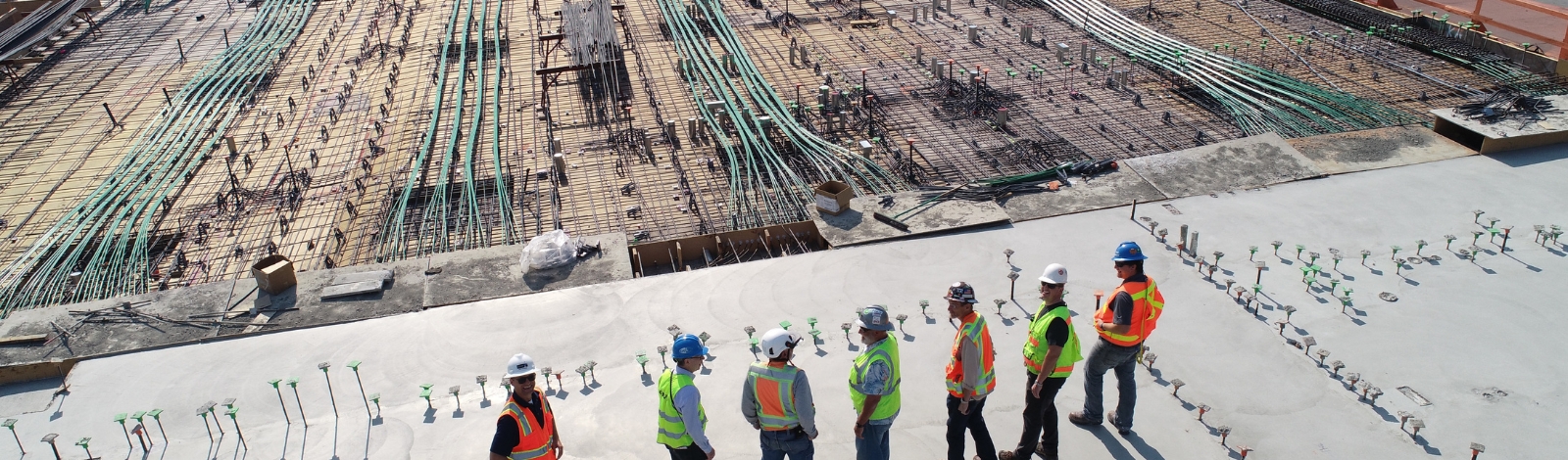 Construction crew in hard hats and high-visibility vests on a concrete deck with exposed rebar